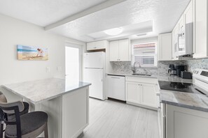 A modern kitchen with white cabinetry, a marble countertop, and a built-in dishwasher. - Casa Blanca - Villa C06 (Sarasota)
