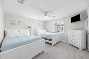 A bedroom with two beds, a ceiling fan, a TV, and artwork on the walls. - Casa Blanca - Villa C06 (Sarasota)