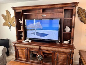 A wooden entertainment center with a flat-screen TV, decorative wall art, and a built-in cabinet. - Casa Blanca - Villa C05 (Sarasota)