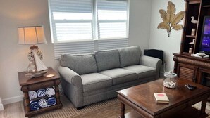 Una sala de estar con un sofá gris, una mesa de centro de madera, una lámpara, una planta decorativa y un televisor.
