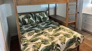 Una cama litera con diseño de hojas tropicales, una escalera de madera y un aparador blanco en la habitación.