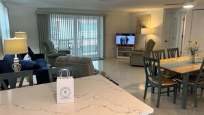 A living room with a television, seating, a dining table, and a bag on the table. - Casa Blanca - Villa A06 (Sarasota)