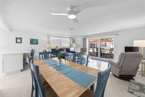Un coin repas avec une table en bois, des chaises bleues et un ventilateur de plafond.