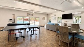 A room with ping pong tables, a sofa, wicker chairs, a ceiling fan, and a TV. - Casa Blanca - Villa A06 (Sarasota)
