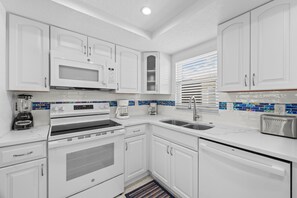 A modern kitchen with white cabinetry, a built-in microwave, a stove, a sink, and a toaster. - Casa Blanca - Villa A06 (Sarasota)