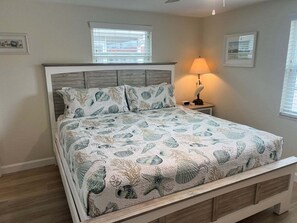 Ein Schlafzimmer mit einem Bett, einem Nachttisch mit Lampe und zwei Fenstern mit Jalousien.