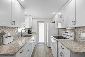 A modern kitchen with white cabinetry, a granite countertop, a built-in oven, and a microwave. - Casa Blanca - Villa A09 (Sarasota)