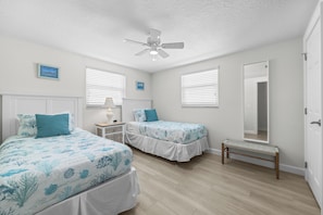 A bedroom with two beds, a ceiling fan, a bedside table with a lamp, and a bench. - Casa Blanca - Villa A09 (Sarasota)