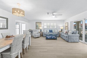 A spacious living room with a dining area, a ceiling fan, and a large window with blinds. - Casa Blanca Villa A11 (Sarasota)