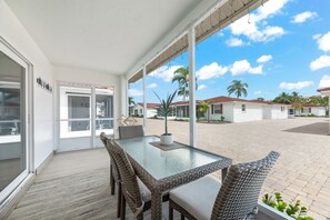 A covered patio area with a glass table and wicker chairs, overlooking a residential area with palm trees and houses. - Casa Blanca Villa A11 (Sarasota)