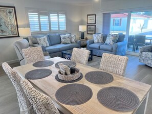 A living room with a dining area, featuring a light blue sofa set, wicker chairs, and a wooden dining table with placemats. - A11 - Where Memories Begin (Sarasota)