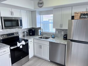 A modern kitchen with white cabinets, stainless steel appliances, a coffee maker, and a sign labeled 'Snacks'. - A11 - Where Memories Begin (Sarasota)