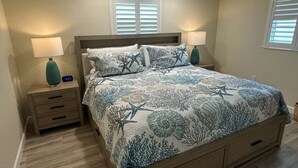 Een slaapkamer met een bed, twee nachtkastjes, een wandklok en een raam met jaloezieën.