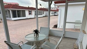 Een overdekt terras met een tafel en stoelen, een plant in pot en uitzicht op een woonwijk met huizen.