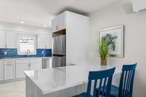Una cocina moderna con armarios blancos, un refrigerador de acero inoxidable, encimera de mármol y una silla azul.
