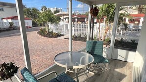 A covered outdoor seating area with a round table and two chairs, a view of a residential street, and a hanging plant. - Casa Blanca - Villa B01 (Sarasota)