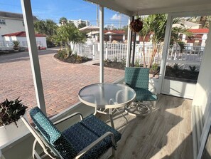 A covered outdoor seating area with a round table and two chairs, a view of a residential street, and a hanging plant. - Casa Blanca - Villa B01 (Sarasota)