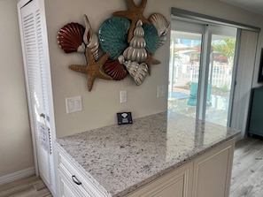 A kitchen with a granite countertop, a decorative shell wall art, a Wi-Fi sign, and a sliding glass door leading to an outdoor area. - B01 - Siesta Key Getaway (Sarasota)