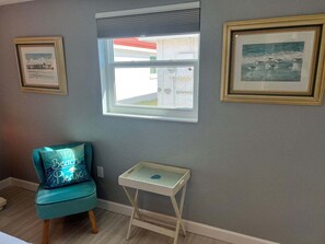 A room with a teal chair, a small white table, and two framed pictures on the wall. - Casa Blanca - Villa B02 (Sarasota)
