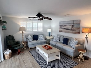A living room with a ceiling fan, two grey sofas, a coffee table, a floor lamp, and a painting on the wall. - B04 - Your Oceanfront Oasis Awaits (Sarasota)