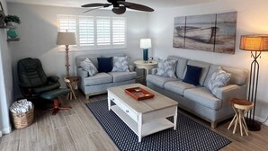 A modern living room with a grey sofa set, a coffee table, a ceiling fan, and a painting on the wall. - Casa Blanca - Villa B04 (Sarasota)