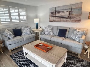 Uma sala de estar com dois sofás cinzas, uma mesa de centro, uma luminária e um quadro na parede.