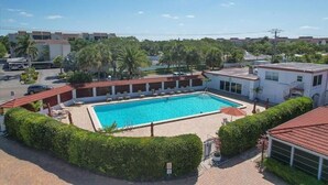 A swimming pool surrounded by greenery, a building with a red roof, and a clear blue sky. - Casa Blanca - Villa B04 (Sarasota)