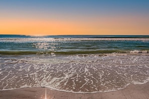 Una playa con olas, cielo despejado y un atardecer.