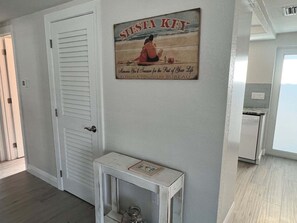 A hallway with a door, a wall-mounted sign, and a small table with a glass jar. - Casa Blanca - Villa B05 (Sarasota)