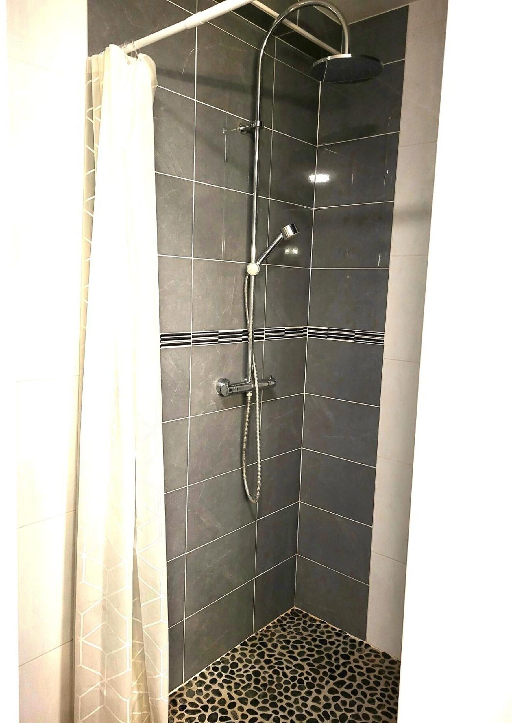 A shower with a curved hose, a handheld showerhead, and a control panel.