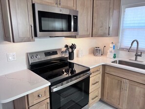 A modern kitchen with stainless steel appliances, wooden cabinets, a built-in oven, and a sink. - B06 - Find Peace in the Sea Breeze (Sarasota)