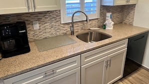 A kitchen with a stainless steel sink, white cabinets, a coffee maker, and a window with blinds. - Casa Blanca - Villa B10 (Sarasota)