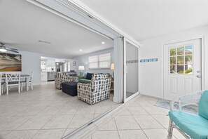 A spacious living area with a sliding glass door leading to a balcony, a kitchen with modern appliances, and a dining area with a table and chairs. - Casa Blanca - Villa B11 (Sarasota)