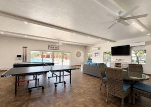 A room with ping pong tables, a sofa, wicker chairs, a ceiling fan, and a TV mounted on the wall. - Casa Blanca - Villa B11 (Sarasota)