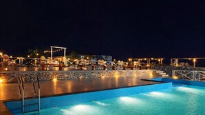 A nighttime swimming pool area with lounge chairs and a stone wall. - Sierra Vista Resort (Talegaon)