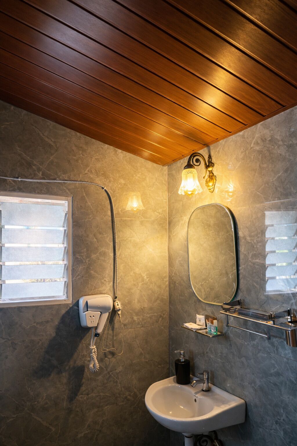 Un baño con techo de madera, una ducha con puerta de cristal, un lavamanos con espejo e iluminación en la pared.