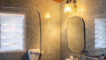 Un baño con techo de madera, una ducha con puerta de cristal, un lavamanos con espejo e iluminación en la pared.