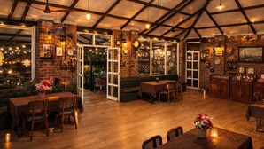 A restaurant with a brick wall, wooden furniture, and a ceiling fan. - Sierra Vista Resort (Talegaon)