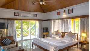 A spacious bedroom with a large bed, a television, a ceiling fan, and a view of the outdoors. - Sierra Vista Resort (Talegaon)