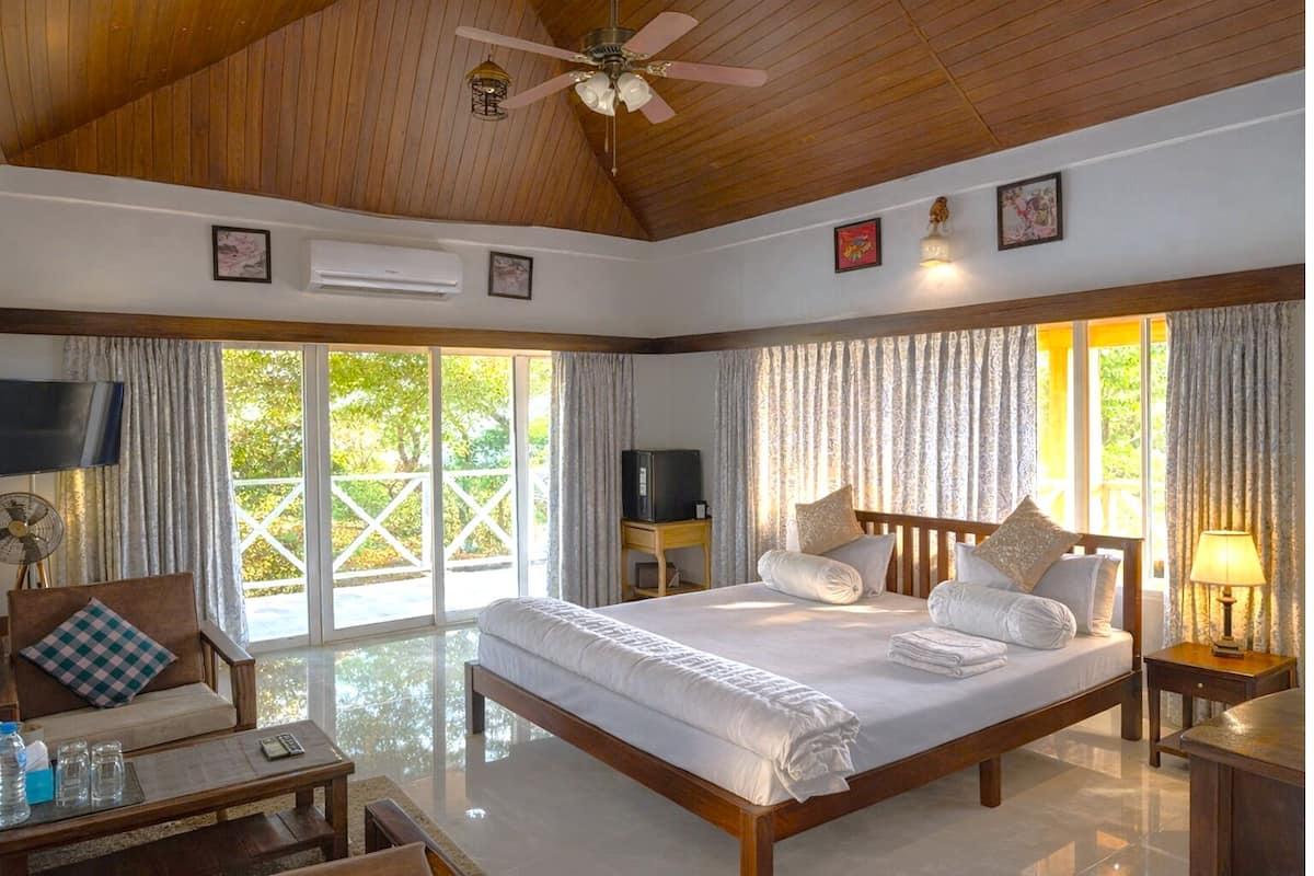 A spacious bedroom with a large bed, a television, a ceiling fan, and a view of the outdoors.