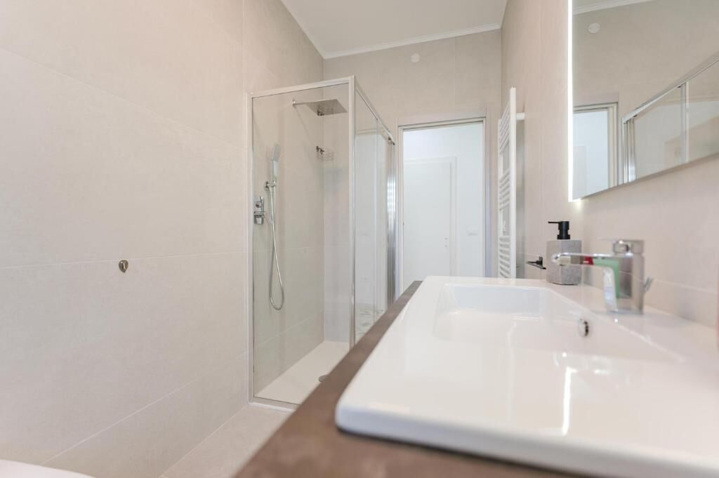 Een moderne badkamer met een douchecabine van glas, een groot wit wastafelmeubel en een spiegel boven de wastafel.