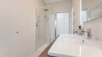 Een moderne badkamer met een douchecabine van glas, een groot wit wastafelmeubel en een spiegel boven de wastafel.