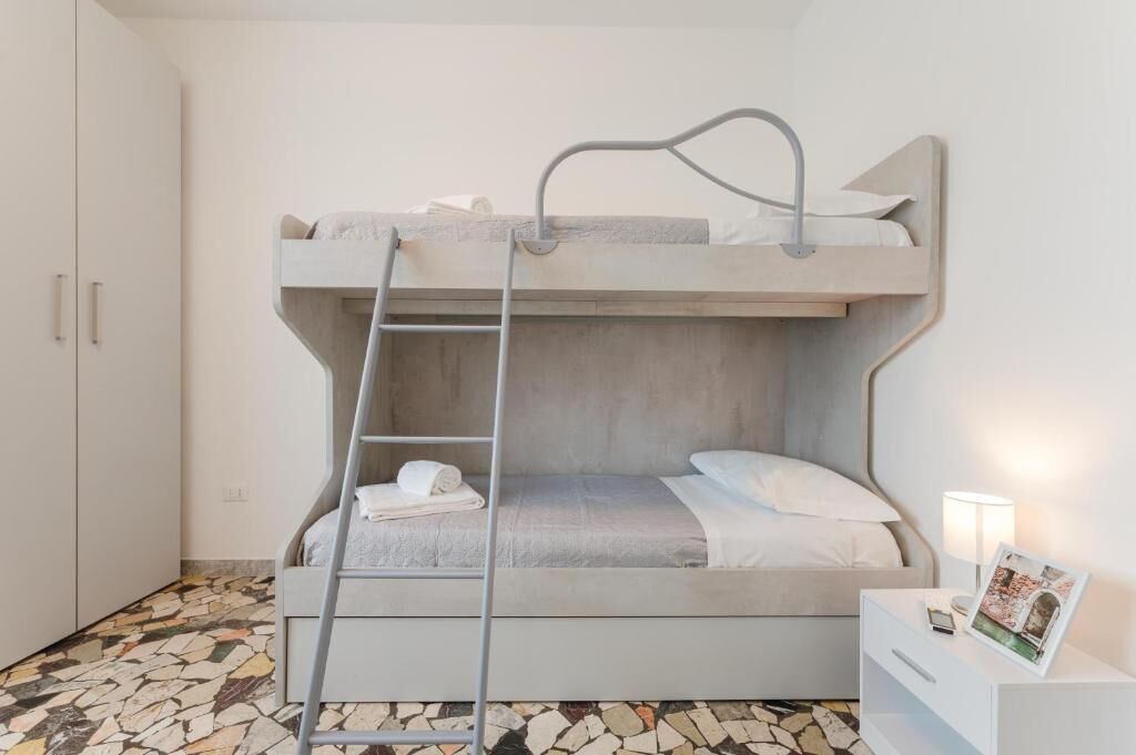 A bunk bed with a ladder, a white bedside table with a lamp, and a patterned floor.