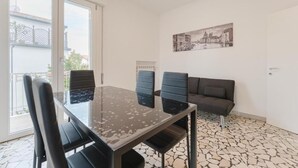 Una stanza con un tavolo in vetro, quattro sedie, un divano e un dipinto che raffigura un panorama urbano.