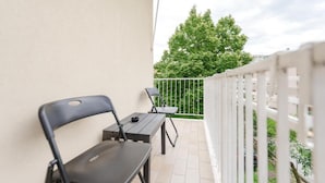 Un balcone con tavolo e sedie, ringhiera bianca e vista su alberi ed edifici.