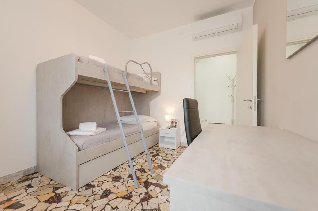Una cama litera con una escalera, una mesita de noche pequeña con una lámpara y una silla.