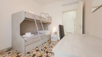 Una cama litera con una escalera, una mesita de noche pequeña con una lámpara y una silla.