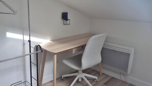 Una stanza con una scrivania in legno, una sedia da ufficio bianca, un termosifone e un lampadario a parete.