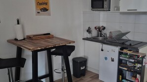 Una cucina compatta con un tavolo in legno, due sgabelli da bar, un forno a microonde, un lavello e un frigorifero.