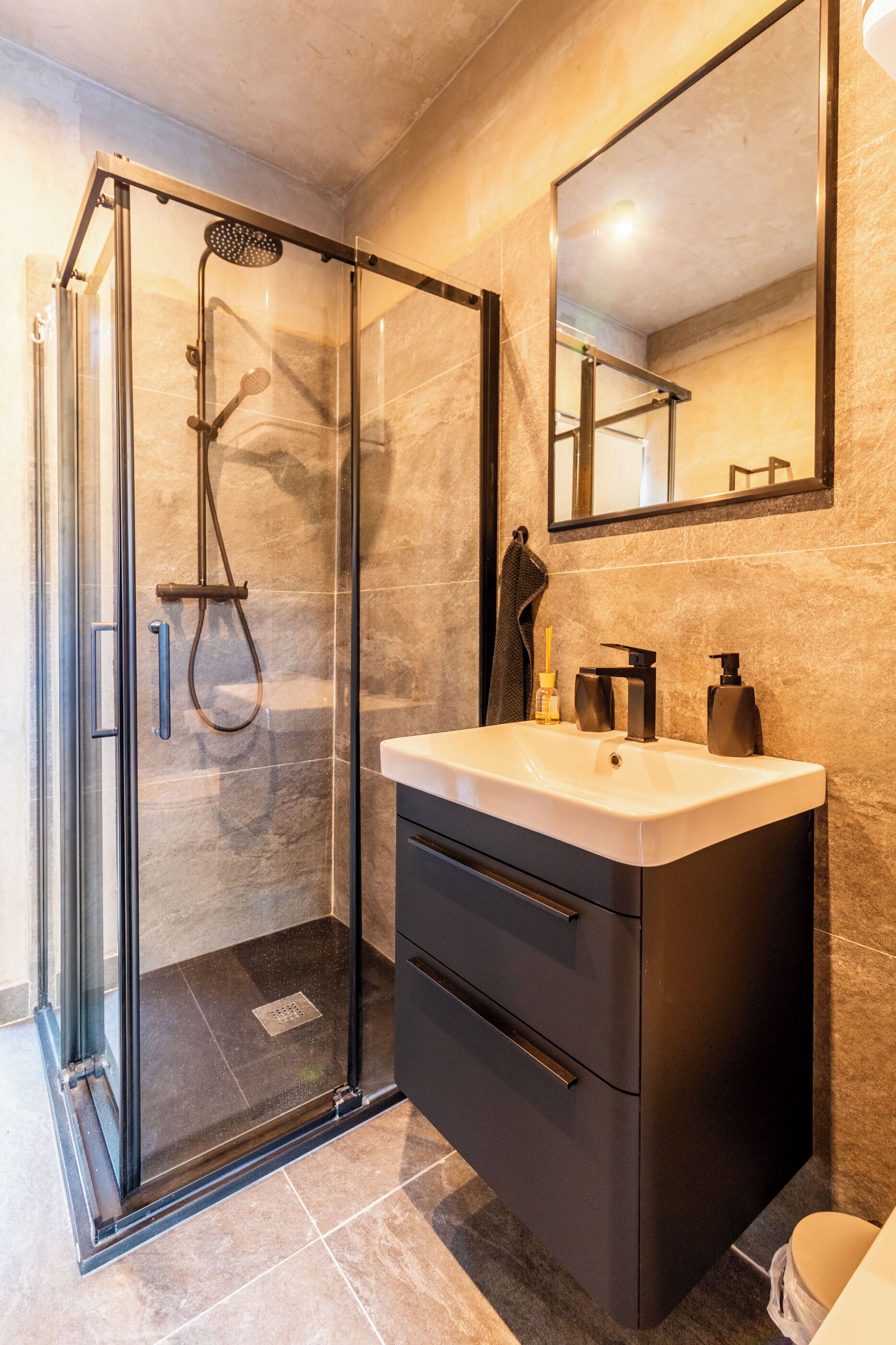 A modern bathroom with a glass-enclosed shower, a white sink, and a dark cabinet.